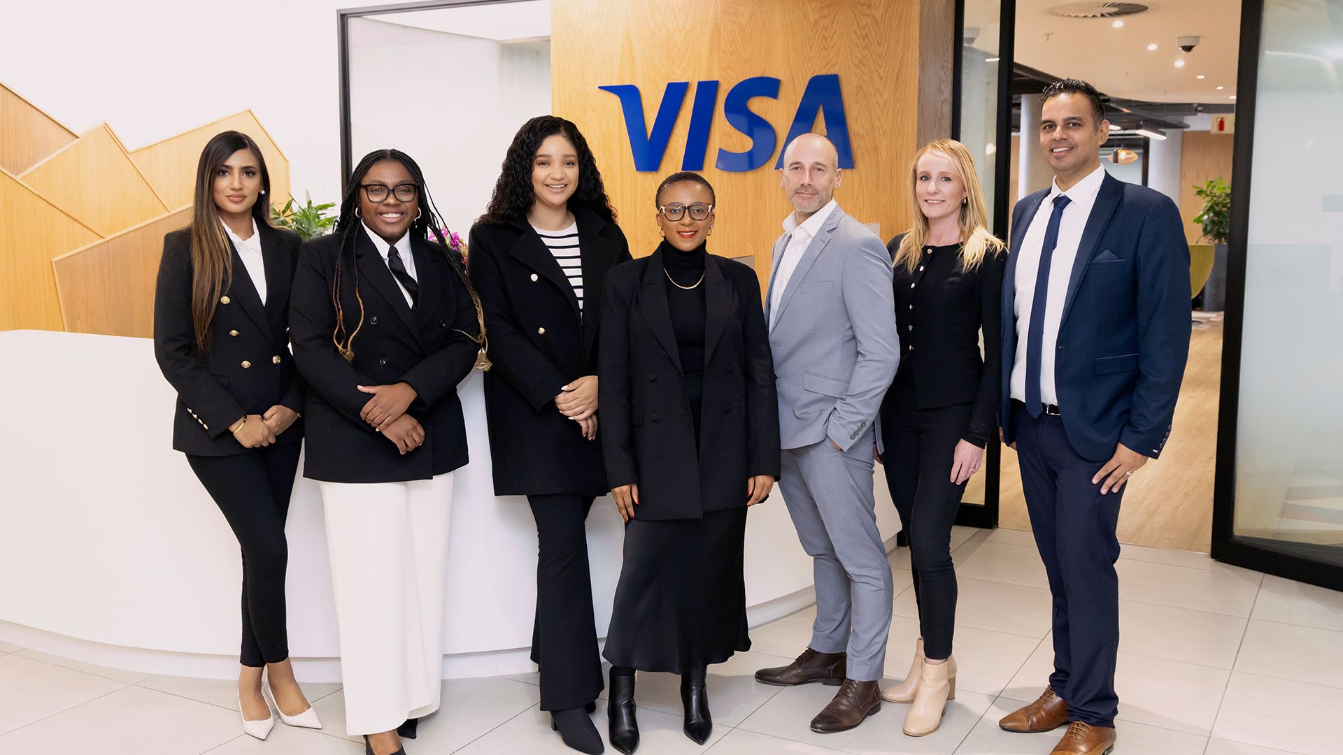 Group of professionals standing together in front of Visa office sign, representing career opportunities.