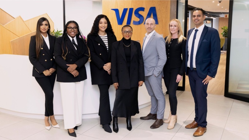 Group of professionals standing together in front of Visa office sign, representing career opportunities.