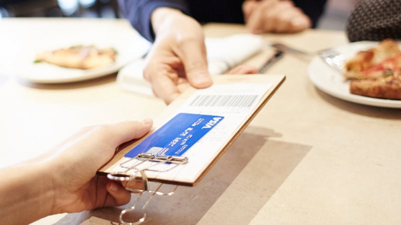 Hand holding a restaurant bill with a Visa credit card.