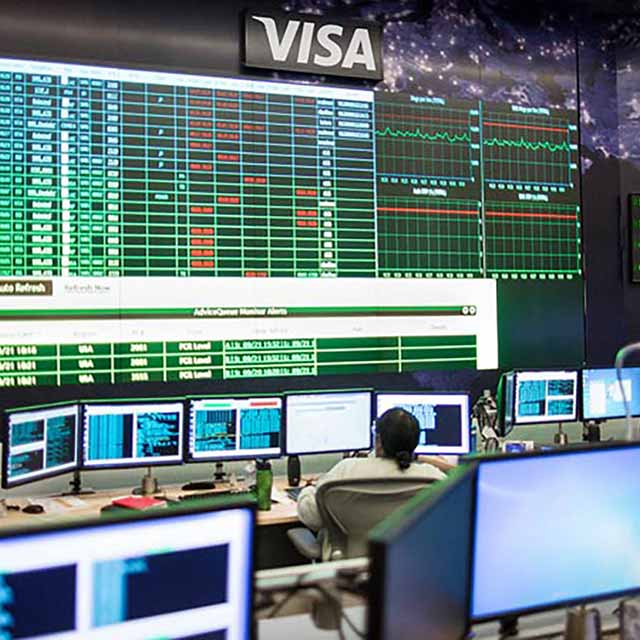 A person is in the visa data center control room and follows the data monitors