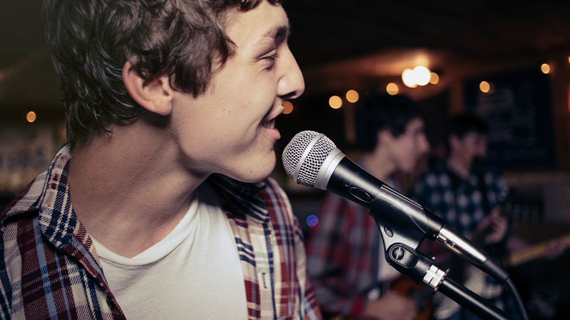 Singer performing with microphone while band plays in the background.